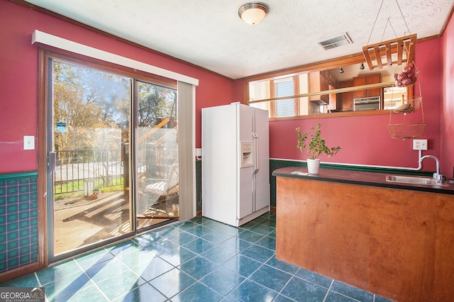 kitchen with a textured ceiling, white fridge with ice dispenser, and sink