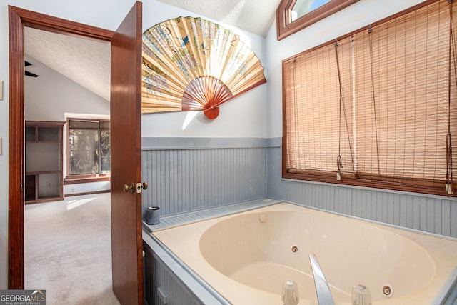 bathroom with a textured ceiling, a bath, and vaulted ceiling