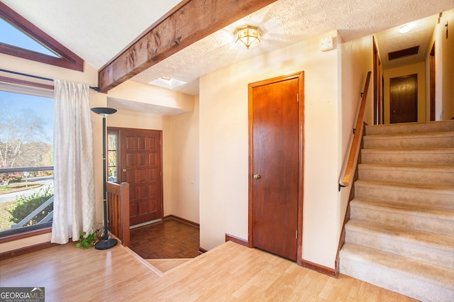 foyer entrance with vaulted ceiling with beams, a textured ceiling, and hardwood / wood-style flooring