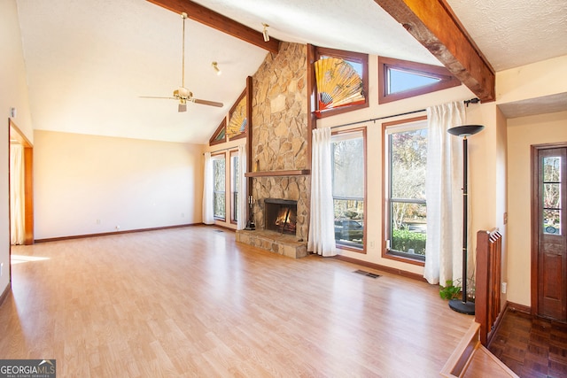 unfurnished living room featuring a textured ceiling, ceiling fan, wood-type flooring, beam ceiling, and a stone fireplace