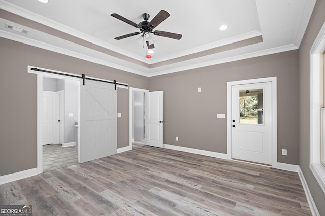 interior space featuring light hardwood / wood-style flooring, crown molding, a barn door, and a raised ceiling