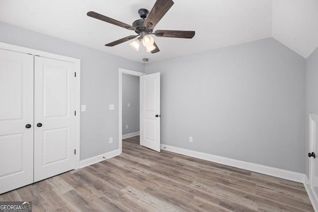 unfurnished bedroom with ceiling fan, light hardwood / wood-style floors, a closet, and vaulted ceiling