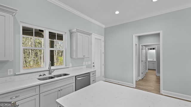 kitchen featuring hardwood / wood-style flooring, ornamental molding, stainless steel dishwasher, light stone counters, and sink