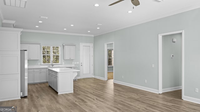 kitchen featuring white cabinetry, stainless steel fridge, a kitchen island, light wood-type flooring, and ornamental molding