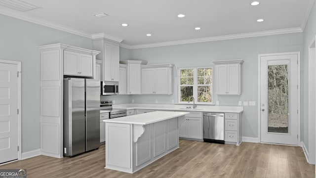 kitchen with white cabinetry, stainless steel appliances, ornamental molding, light hardwood / wood-style flooring, and a center island