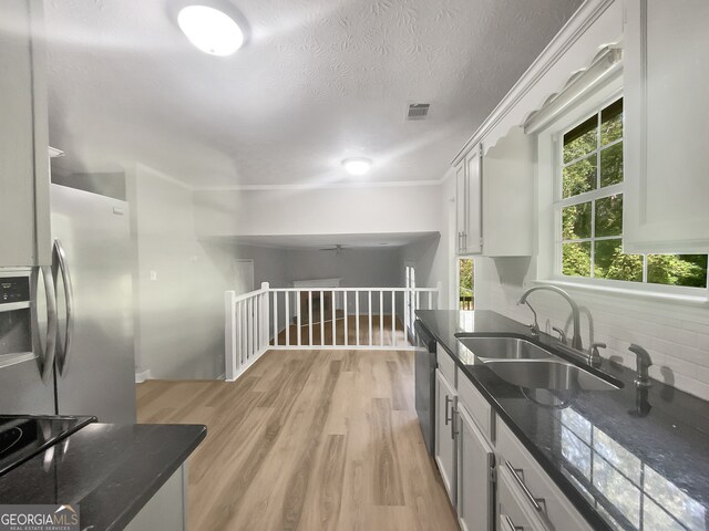 kitchen with backsplash, appliances with stainless steel finishes, white cabinetry, light wood-type flooring, and sink