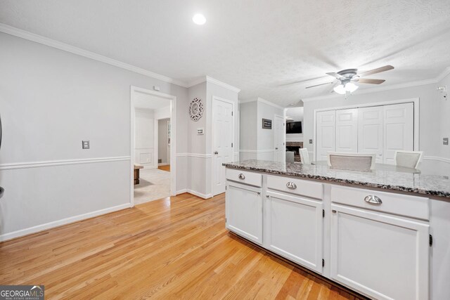 kitchen with white cabinets, ceiling fan, light wood-type flooring, light stone countertops, and ornamental molding