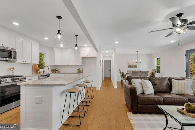 kitchen with light stone counters, white cabinets, stainless steel appliances, and light wood-type flooring