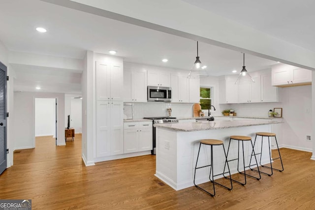 kitchen with white cabinets, appliances with stainless steel finishes, light stone countertops, light hardwood / wood-style floors, and decorative light fixtures