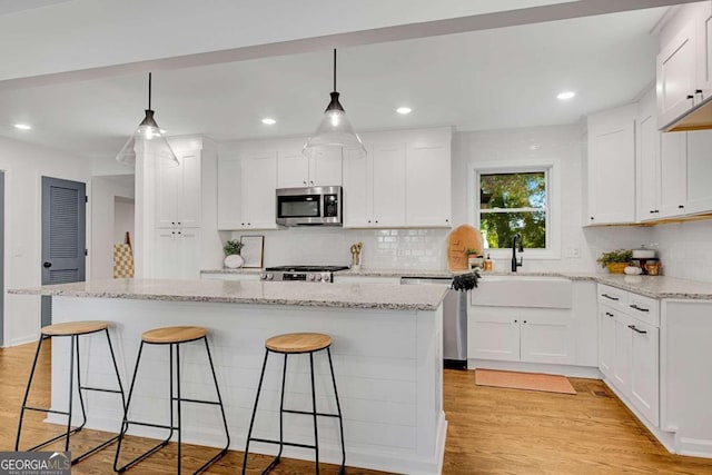 kitchen featuring a kitchen island, appliances with stainless steel finishes, decorative light fixtures, and white cabinetry