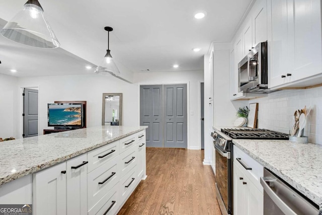 kitchen with appliances with stainless steel finishes, hanging light fixtures, white cabinetry, light stone counters, and light hardwood / wood-style flooring