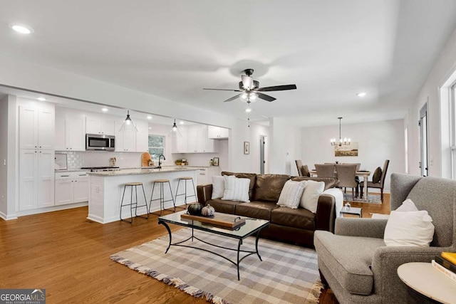 living room featuring sink, ceiling fan with notable chandelier, and light hardwood / wood-style floors