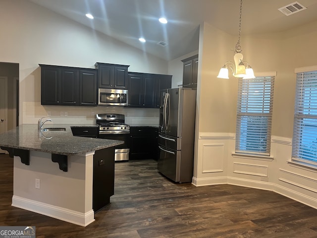 kitchen featuring a breakfast bar, appliances with stainless steel finishes, dark stone countertops, hanging light fixtures, and dark wood-type flooring