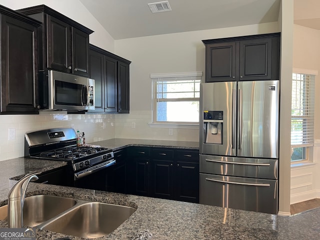 kitchen with sink, appliances with stainless steel finishes, dark stone countertops, lofted ceiling, and decorative backsplash