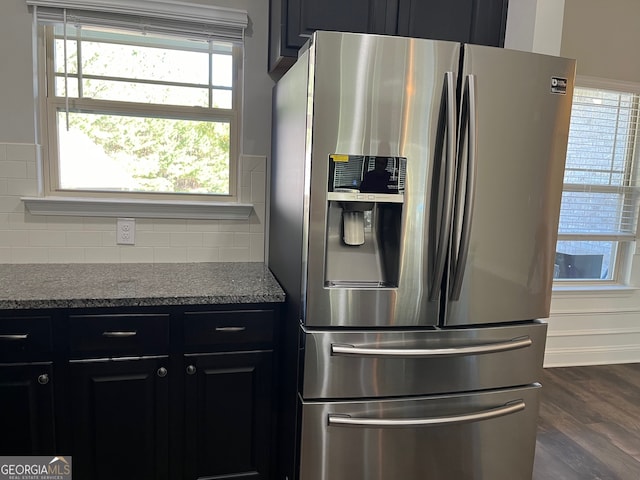 kitchen with dark wood-type flooring, light stone countertops, stainless steel fridge with ice dispenser, and decorative backsplash