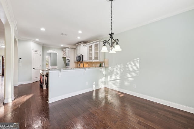 kitchen with dark hardwood / wood-style flooring, kitchen peninsula, hanging light fixtures, crown molding, and a breakfast bar