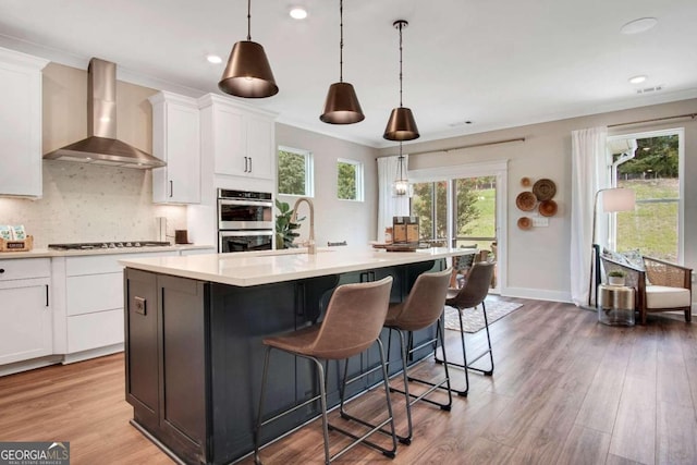 kitchen with an island with sink, wall chimney range hood, white cabinets, and dark hardwood / wood-style flooring