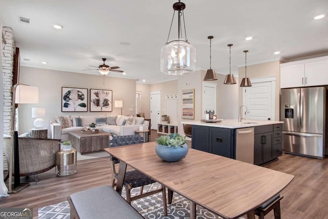 kitchen featuring light hardwood / wood-style flooring, stainless steel appliances, hanging light fixtures, and an island with sink