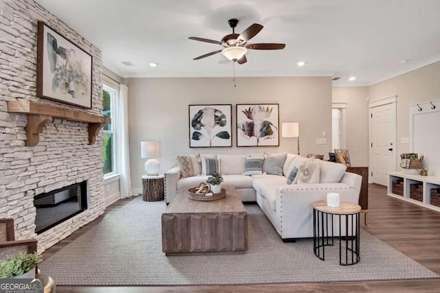 living room featuring a stone fireplace, dark hardwood / wood-style floors, ceiling fan, and ornamental molding