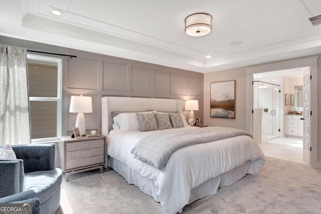 carpeted bedroom featuring ornamental molding, a tray ceiling, and ensuite bath