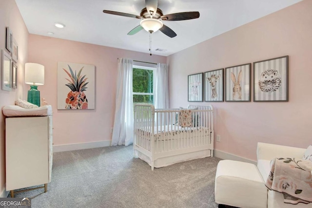 carpeted bedroom featuring a nursery area and ceiling fan