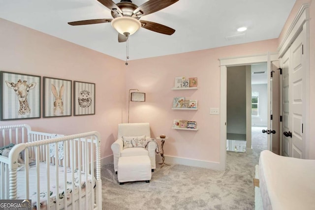 carpeted bedroom featuring a crib and ceiling fan