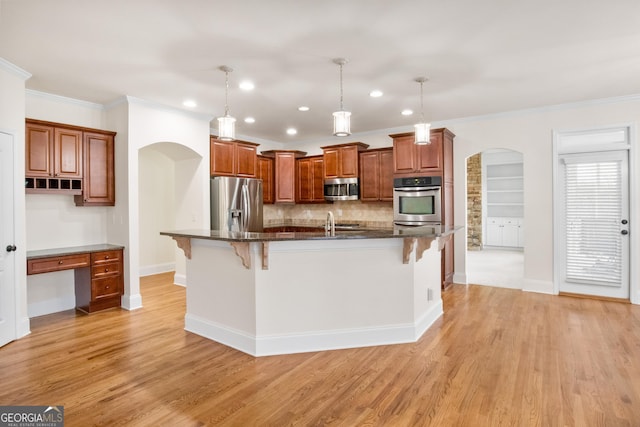 kitchen with crown molding, a breakfast bar area, appliances with stainless steel finishes, a center island with sink, and decorative light fixtures