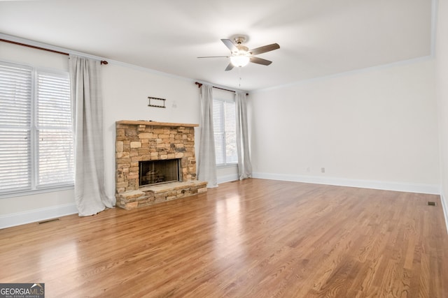 unfurnished living room with ornamental molding, a healthy amount of sunlight, a stone fireplace, and light hardwood / wood-style flooring