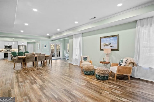 sitting room featuring a tray ceiling, light hardwood / wood-style flooring, ornamental molding, and french doors