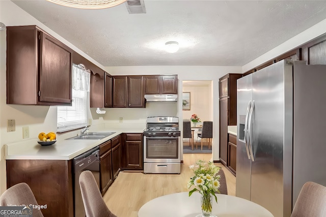 kitchen featuring dark brown cabinetry, sink, a textured ceiling, light hardwood / wood-style flooring, and stainless steel appliances