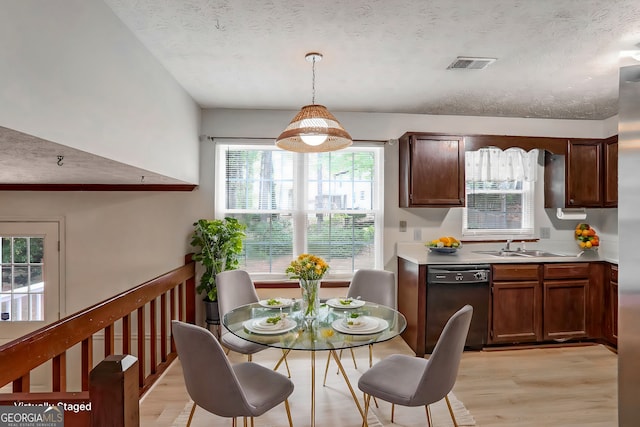 kitchen featuring sink, black dishwasher, a textured ceiling, decorative light fixtures, and light wood-type flooring