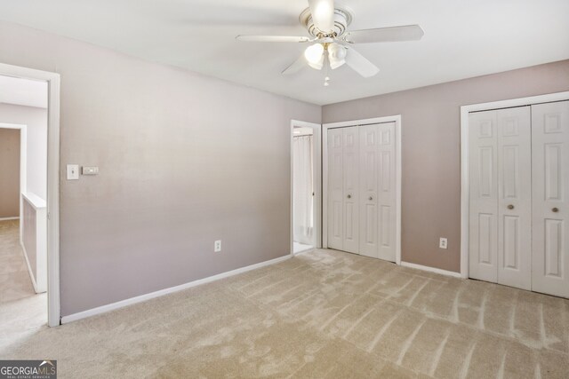 unfurnished bedroom with ceiling fan, light carpet, and two closets