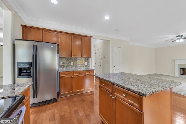 kitchen with ornamental molding, a center island, light wood-type flooring, appliances with stainless steel finishes, and light stone counters