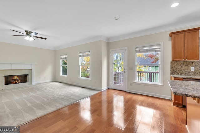 unfurnished living room with light hardwood / wood-style floors, ornamental molding, a tile fireplace, and ceiling fan