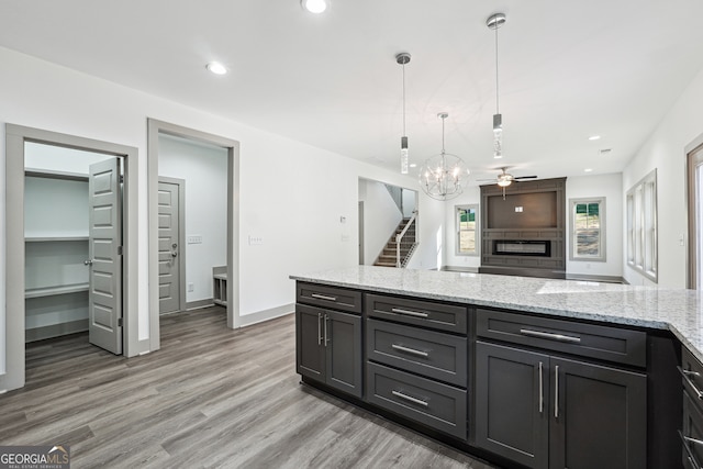 kitchen featuring pendant lighting, light stone counters, hardwood / wood-style flooring, and ceiling fan