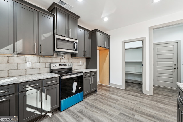 kitchen featuring decorative backsplash, light stone countertops, stainless steel appliances, and light wood-type flooring