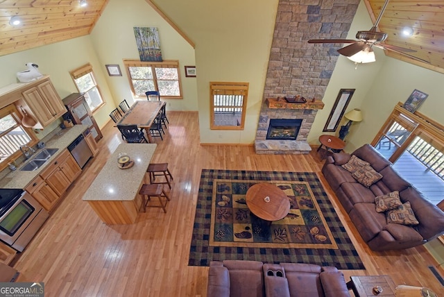 living room with a stone fireplace, high vaulted ceiling, sink, wood ceiling, and light hardwood / wood-style floors