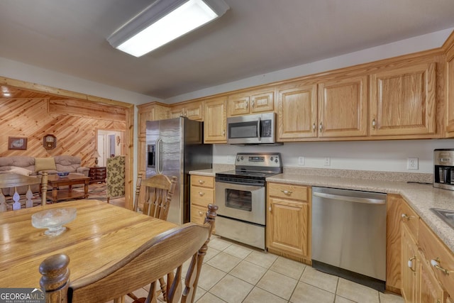 kitchen featuring stainless steel appliances, light countertops, light tile patterned flooring, and wooden walls