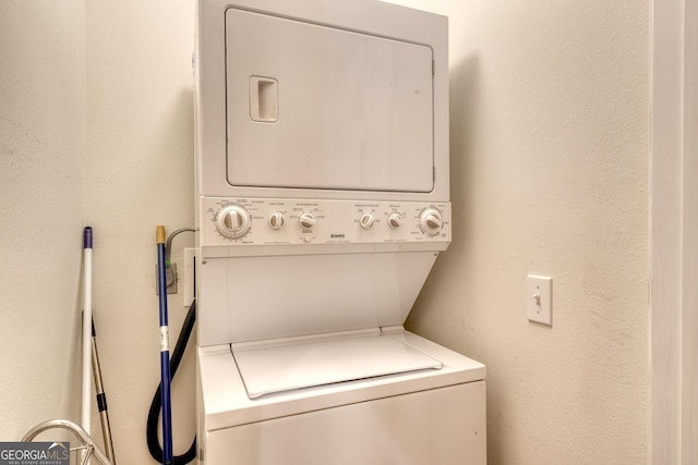 clothes washing area featuring a textured wall, stacked washer and dryer, and laundry area