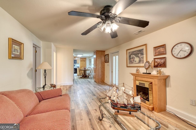 living room with ceiling fan, a fireplace, visible vents, baseboards, and light wood-type flooring