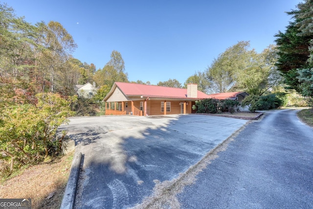 ranch-style home featuring covered porch, driveway, and a chimney