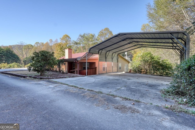 view of side of home featuring driveway, a chimney, and a detached carport