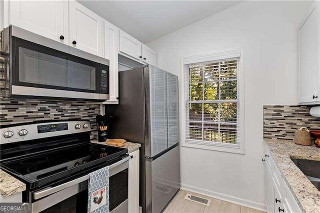 kitchen featuring white cabinetry, light stone countertops, stainless steel appliances, and backsplash