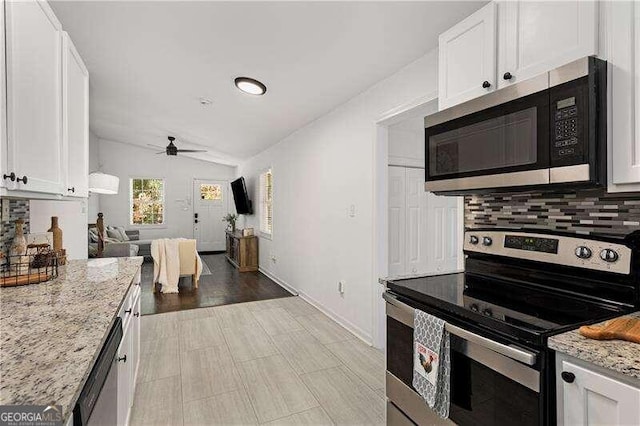 kitchen featuring white cabinetry, stainless steel appliances, lofted ceiling, light stone counters, and decorative backsplash