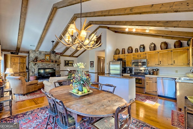 dining area with sink, light wood-type flooring, a fireplace, lofted ceiling with beams, and a notable chandelier