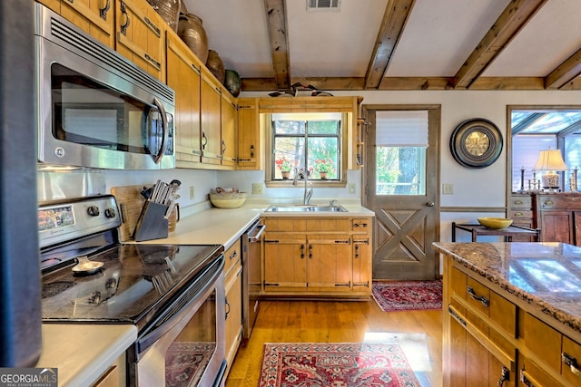 kitchen featuring light stone countertops, sink, light wood-type flooring, stainless steel appliances, and beamed ceiling