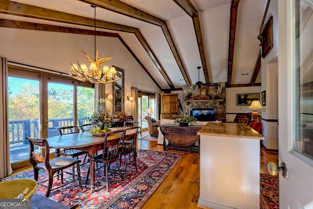 dining space featuring a notable chandelier, a stone fireplace, light hardwood / wood-style flooring, and vaulted ceiling with beams