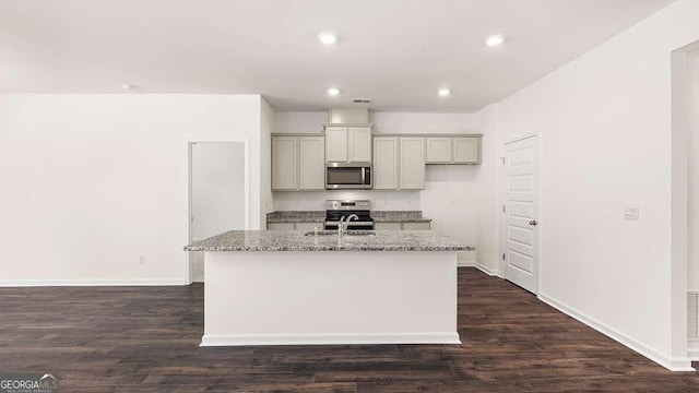 kitchen with dark wood-type flooring, stainless steel appliances, light stone countertops, and a kitchen island with sink