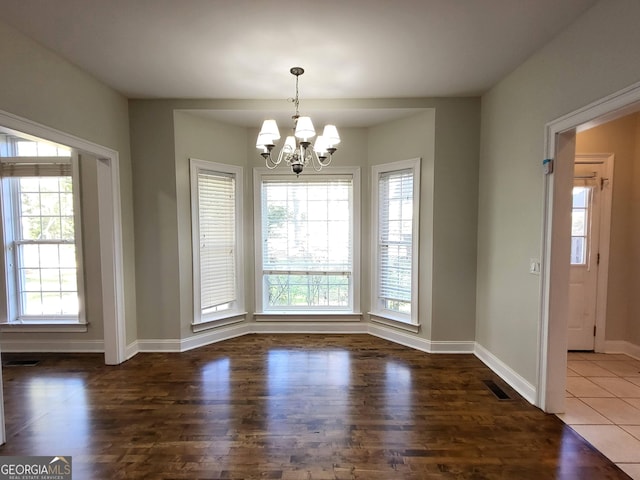 unfurnished dining area featuring dark wood-style flooring, visible vents, baseboards, and an inviting chandelier