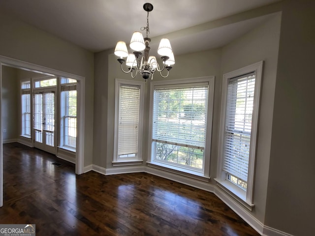 unfurnished dining area featuring baseboards, dark wood-type flooring, visible vents, and a notable chandelier